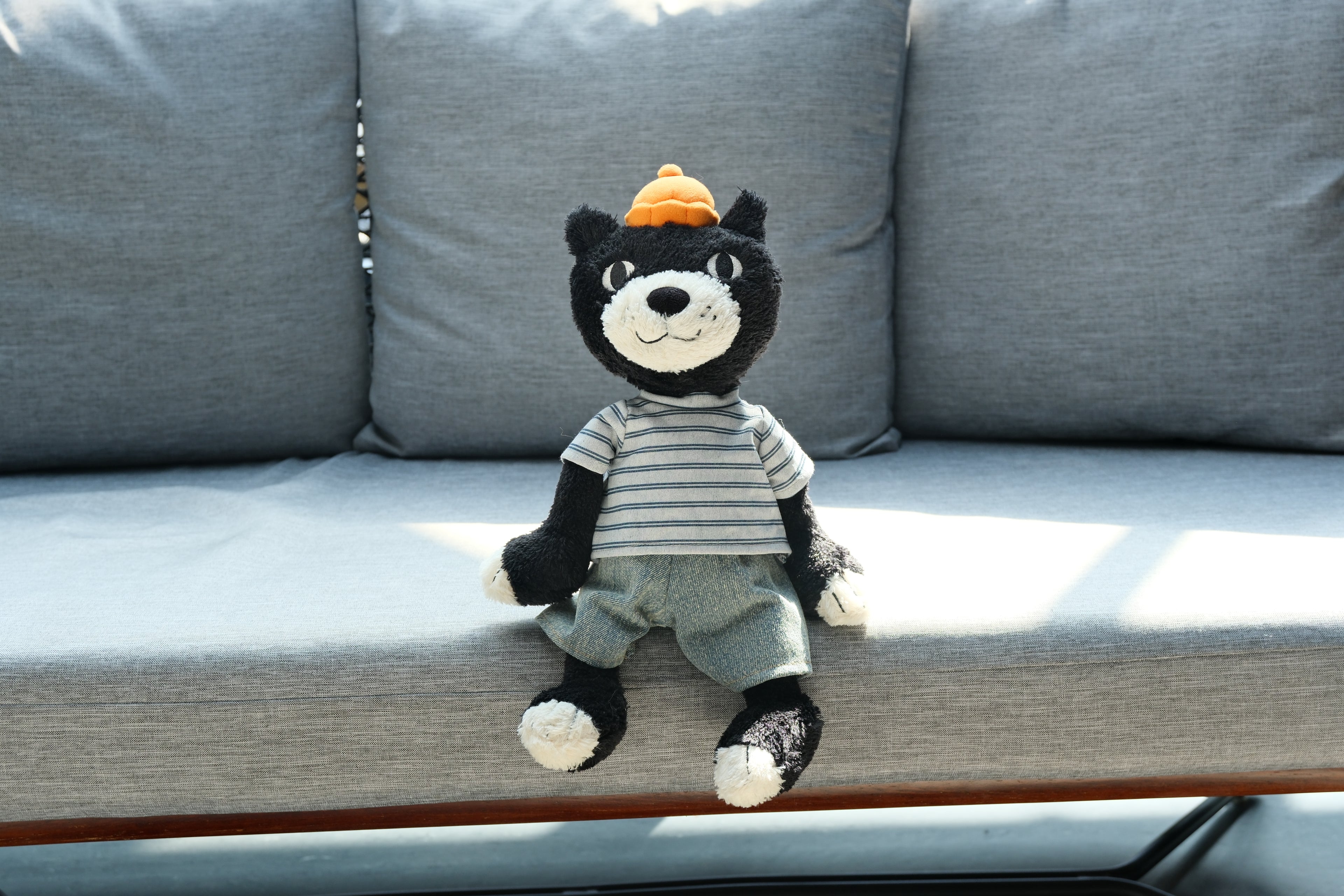 Jack plush wearing a striped T-shirt and denim trousers while seated on a gray outdoor sofa